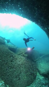 Freediver swims underwater in the sea and explores the rocky bottom