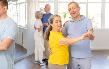 Positive senior woman and man practicing tango dance moves as a couple during a group celebration...