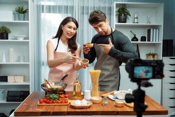 Couple chef influencers on cooking show presenting ingredient of spaghetti, meat, chilli, tomato, garlic and seasoning sauce's homemade special recipe recording on camera on live channel. Postulate.