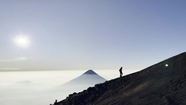 Hiking with a silhouette of a hiker against the backdrop of a volcano towering over the clouds in the background. Voldaco de Fuego , Acatenango antigua Guatemala