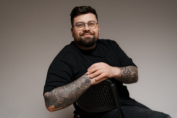 Confident, tattooed young man with glasses smiling, seated in a modern minimalist setting