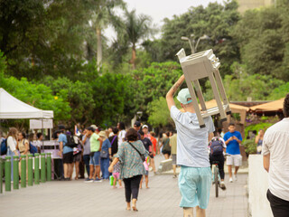 Street Cuisine on the Move: A man strolling through Kennedy Park in Peru, carrying a street-style fryer. A unique glimpse of mobile culinary culture in the heart of the park. - obrazy, fototapety, plakaty