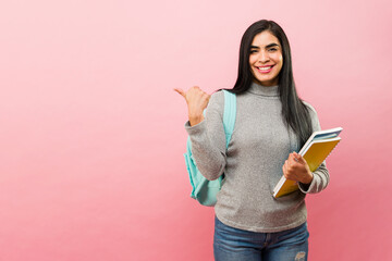 Attractive hispanic woman studying college pointing to a pink copy space ad