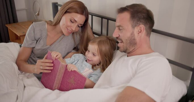 Smiling parents reading a story to their daughter in bed