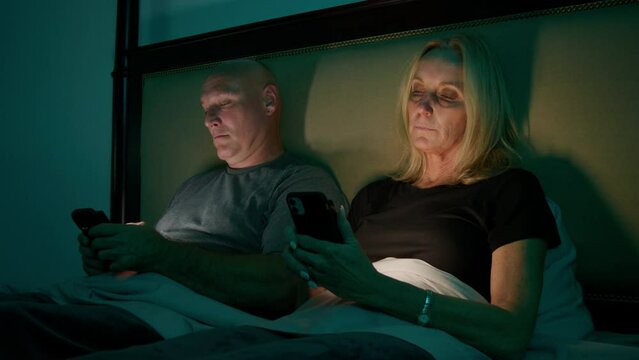 A married couple scroll on their smartphones in bed