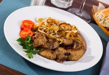 Fried rabbit liver served on white plate with grilled onion and cherry tomatoes