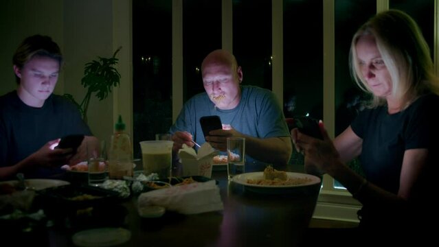 Man binge eats pasta while scrolling his phone at a family dinner