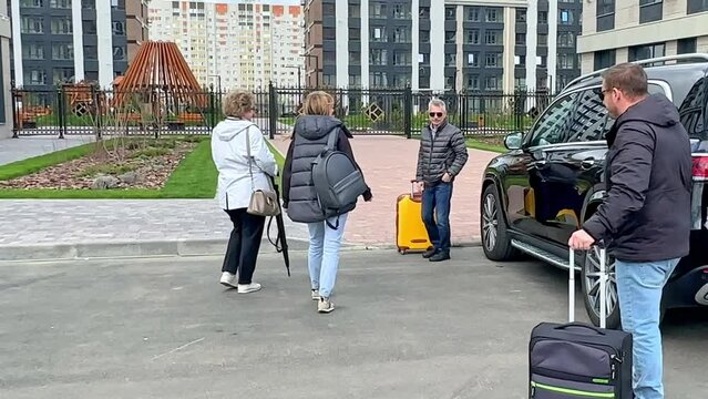 Parents and children take out heavy suitcases package from open trunk of black car on a street. Happy multi generations family is coming back home after road trip. Concept vacation, family travelling