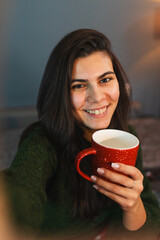 A young girl or woman is taking a selfie while getting up from bed drinking coffee or tea in blanket cozy room	
