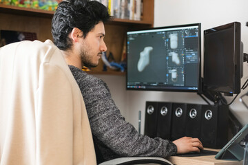 Latin man with a beard works at home with a computer with two monitors and a sound system near a tablet