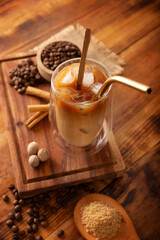 Iced coffee served in a double-walled glass cup and metal straw, a cold summer drink prepared with ice cubes and spices, cinnamon, nutmeg, vanilla, muscovado sugar and cream.
