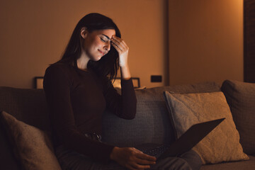 Stressed woman at late night having strong terrible headache attack after computer laptop study, sleepy exhausted girl suffering from chronic migraine massaging temples to relieve head ache tension.