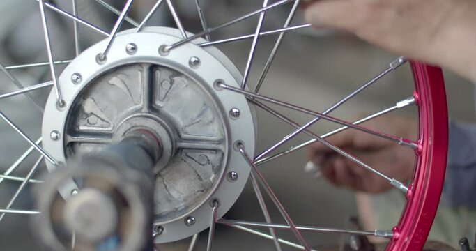 Side view An Asian male working motorcycle wheel has spokes weave up on mechanic new steel wheel with Motorcycle spokes wheel alignment machine tool.