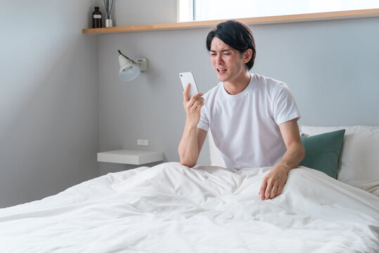 朝寝起きにスマートフォンを見る若いアジア人男性（時刻・アラーム・遅刻・寝坊）
