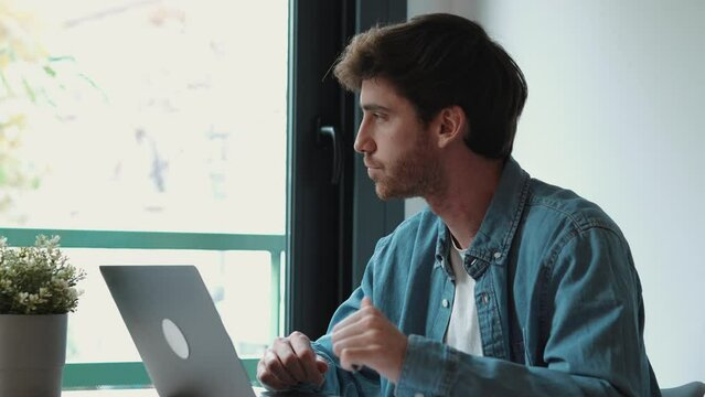 Thoughtful businessman touching chin, pondering ideas or strategy, sitting at wooden work desk with laptop, freelancer working on online project, student preparing for exam at home

