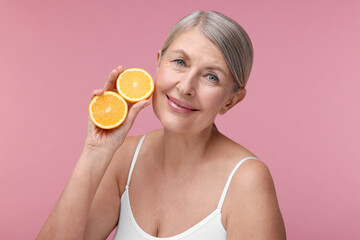 Beautiful woman with halves of orange rich in vitamin C on pink background