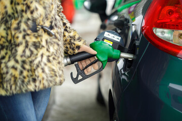 Woman fills petrol into her car at a gas station in winter - obrazy, fototapety, plakaty