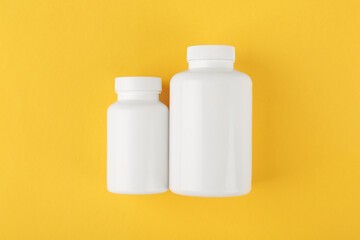 White medical bottles on yellow background, top view