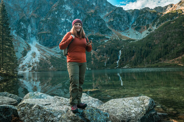 Shot of woman traveler relaxing alone travel in adventure vacation with backpack enjoying standing on the top of the mountain near Famous mountains lake Morskie oko or sea eye lake In High Tatras.  - obrazy, fototapety, plakaty