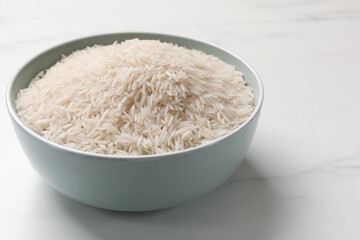 Raw basmati rice in bowl on white marble table, space for text