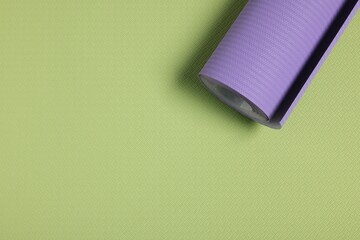 One violet wallpaper roll on green sample, top view. Space for text