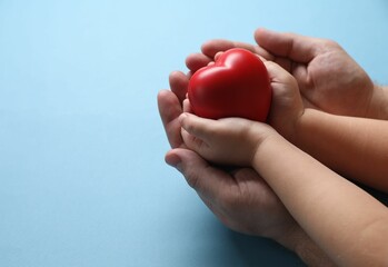 Father and his child holding red decorative heart on light blue background, closeup. Space for text