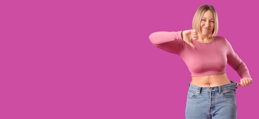 Displeased woman in loose jeans showing thumb-down on magenta background with space for text....