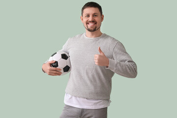 Handsome man with soccer ball showing thumb-up on green background