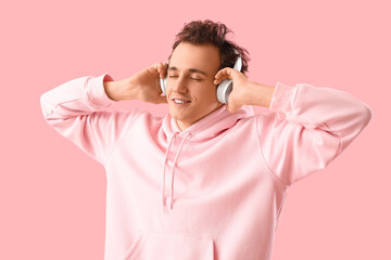 Young man in headphones listening to music on pink background