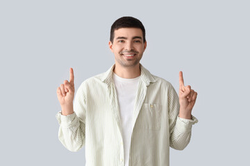 Young man pointing at something on light background