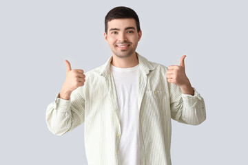 Young man showing thumbs-up on light background