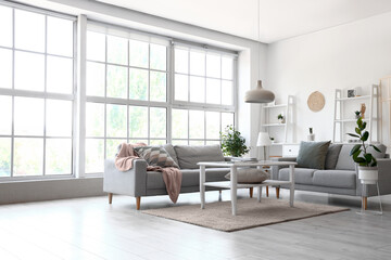 Interior of light living room with grey sofas and coffee table near big window