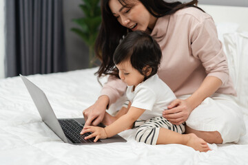 toddler baby with mother using and typing on laptop computer on bed