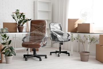 Interior of office with chairs wrapped in stretch film and cardboard boxes on moving day