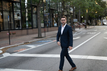 Businessman with backpack walking in city. Side view of male entrepreneur in classy suit and with takeaway drink walking along crosswalk while commuting to work in morning. businessman in the street