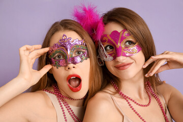 Beautiful young women in carnival masks on lilac background © Pixel-Shot