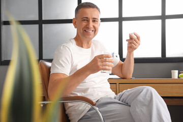 Middle-aged man with glass of water taking pills at home