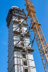 Fototapeta na wymiar Elevator shaft of a new city high rise under construction, yellow crane on a sunny blue sky day 