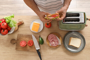 Middle-aged man with tasty sandwich, toaster and ingredients in kitchen, top view
