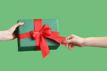 Female hands holding Christmas present on green background