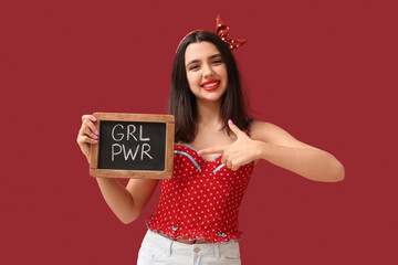 Beautiful young happy pin-up woman pointing at blackboard with text GIRL POWER on red background