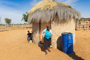 village african woman in front of a shack with thatched roof, in a sunny day outdoors