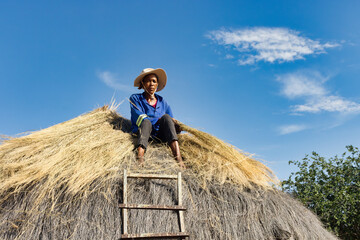 Naklejka na ściany i meble village african woman repairing a thatched roof, manual labor in a sunny day outdoors