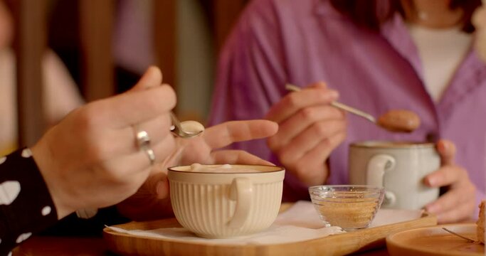 Close-up of feminine hands delicately swirling coffee spoon through frothy foam cappuccino or cocoa. Hands with elegant rings add touch of sophistication to scene, embodying grace of lady's touch. 