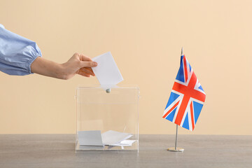 Voting young woman with UK flag near ballot box on table at polling station