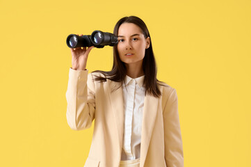 Young businesswoman with binoculars on yellow background