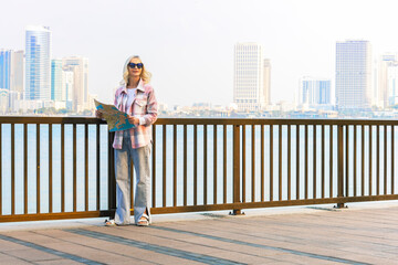 Happy mature woman traveler looks at the map while walking along the waterfront.  travel and tourism concept.