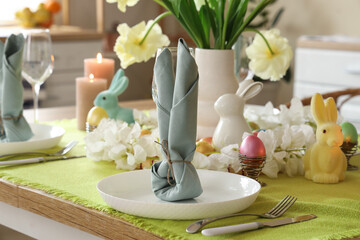 Festive table setting with candles, Easter bunny and vase of yellow tulips in kitchen, closeup