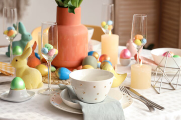 Stylish table setting with candles, painted eggs and Easter bunnies