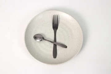 Empty plate with spoon and fork on a white background, representing fasting during Ramadan and the...